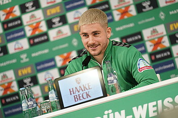 null Romano Schmid sitzt lächelnd auf dem PK-Podium.