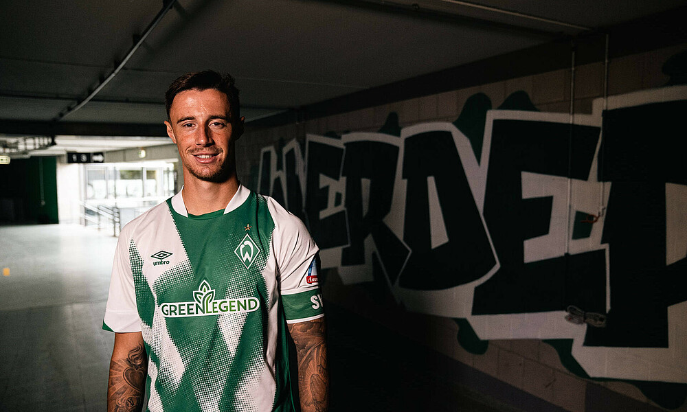 null Marco Friedl steht im Home-Trikot vor einer Wand mit einem Werder-Graffiti