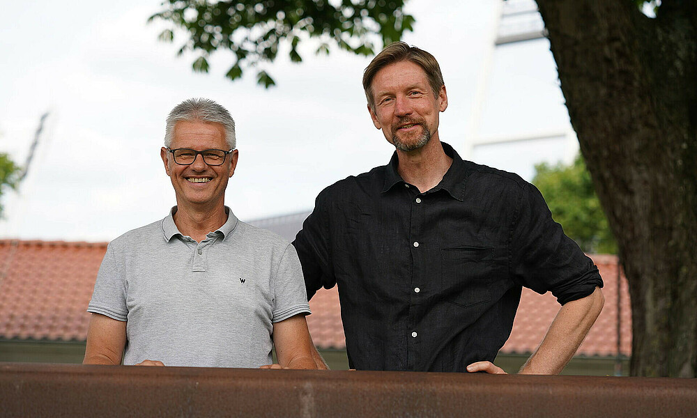 Ralf Heskamp und Marc Dommer stehen zusammen und lächeln in die Kamera