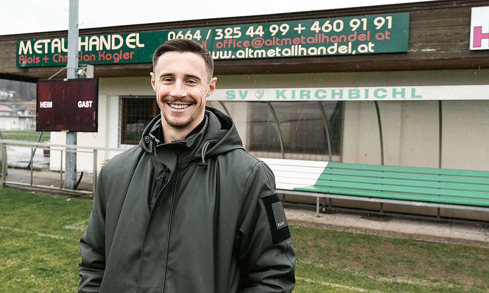 Marco Friedl lächelt vor der Ersatzbank des SV Kirchbichl. 