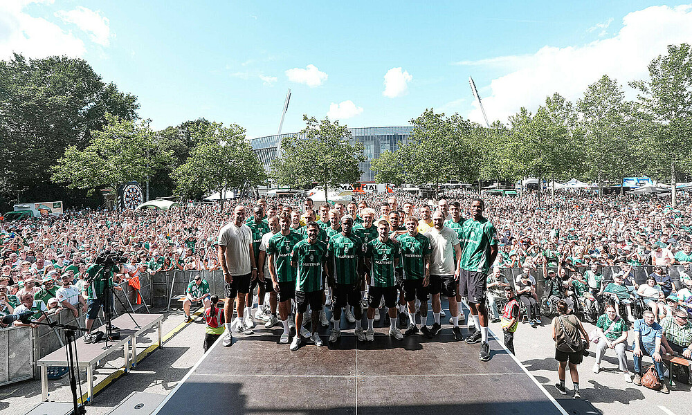 Mannschaftsbild der Bundesliga-Mannschaft auf einer Bühne vor dem Weserstadion. Im Hintergrund sind viele Fans. 