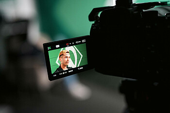 Man sieht Mio Backhaus, wie er spricht über den Bildschirm einer Kamera. 