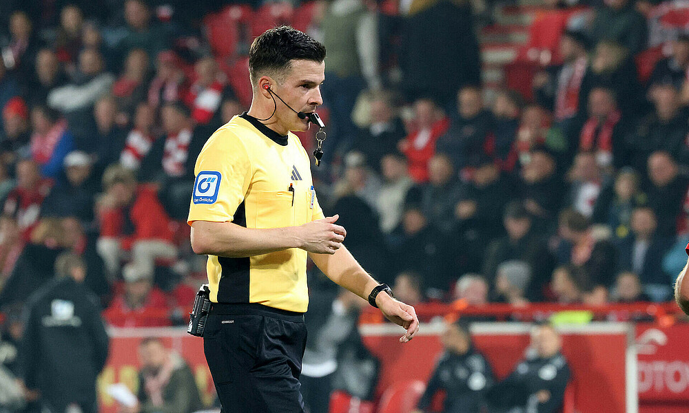 Harm Osmers im gelbfarbenen Schiedsrichtertrikot mit der Pfeife im Mund