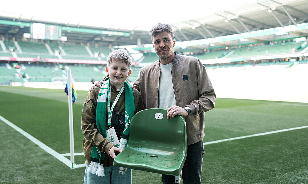 null Tamme Jeß steht mit seinem Geschenk, einer Sitzschale aus dem Weserstadion, neben Clemens Fritz