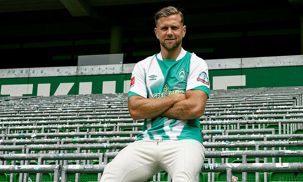 Niclas Füllkrug sitzt im neuen Home-Trikot auf einem Wellenbrecher in der Ostkurve.