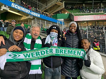 Fünf Personen stehen im Weserstadion und halten einen Werder-Schal hoch