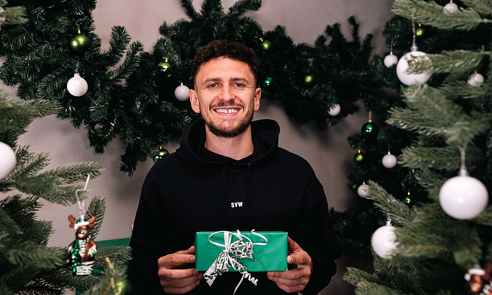 Milos Veljkovic hält ein Geschenk und lächelt.