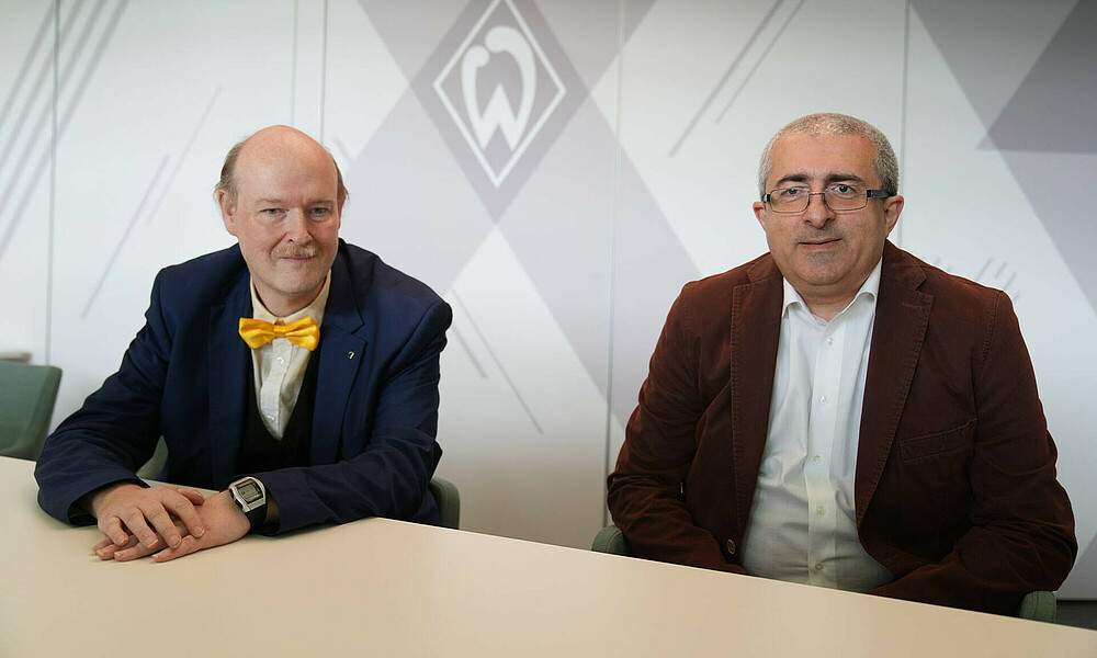null Dr. Oliver Höpfer und David Lobzhanidze sitzen am Tisch und lächeln in die Kamera.