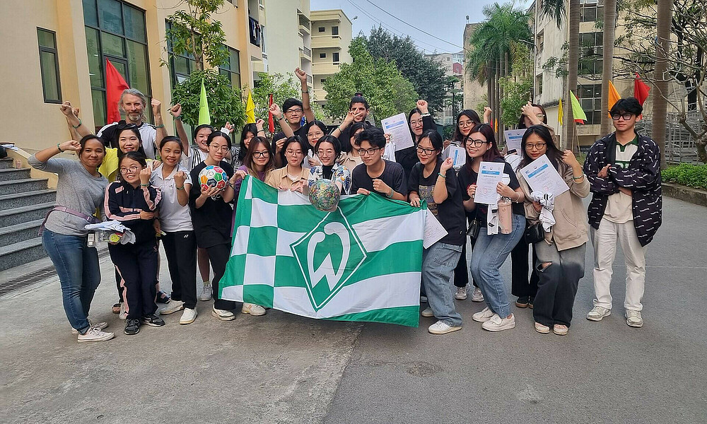 Gruppenfoto der Teilnehmer:innen des Workshops, die eine Werder-Fahne hochhalten.