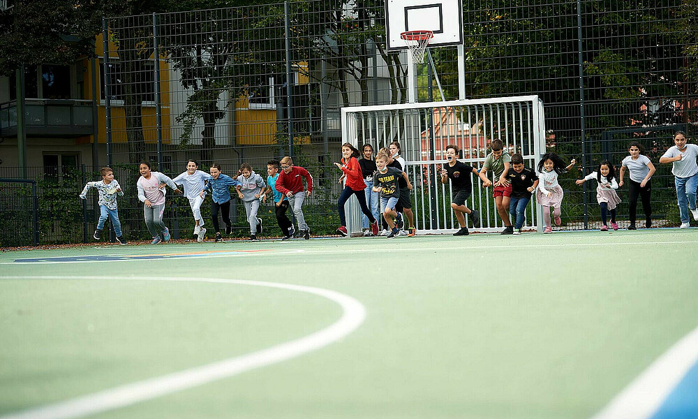 Auf dem Bild sieht man mehrere rennende Kinder auf einem Soccer-Court.