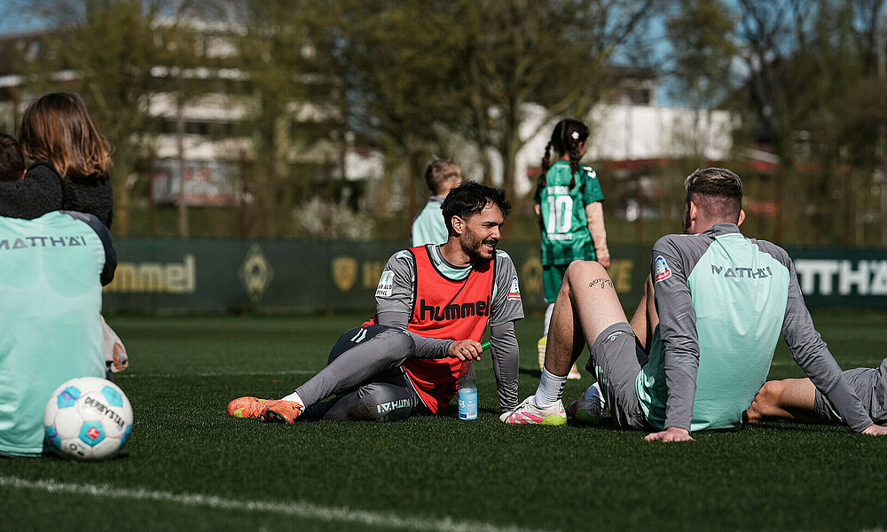 Leonardo Bittencourt sitzt im Trainingsleibchen auf dem Platz, im Hintrgrund sind seine Kinder von hinten