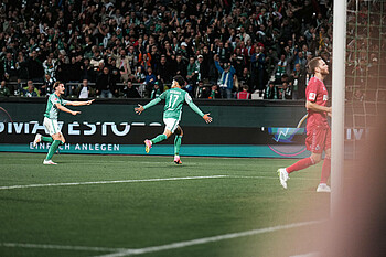 Justin Njinmah von hinten, wie er mit ausgestreckten Armen jubelnd läuft.