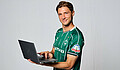 null Niklas Stark steht vor einem weißen Hintergrund. Er hält einen Laptop in der Hand.