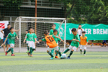 Kinder in grünen Trikots spielen Fußball.