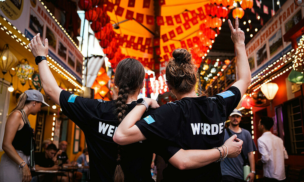 Zwei Werder-Spielerinnen mit dem Rücken zur Kamera an einer bekannten Straße in Hanoi auf den Eisenbahngleisen. 