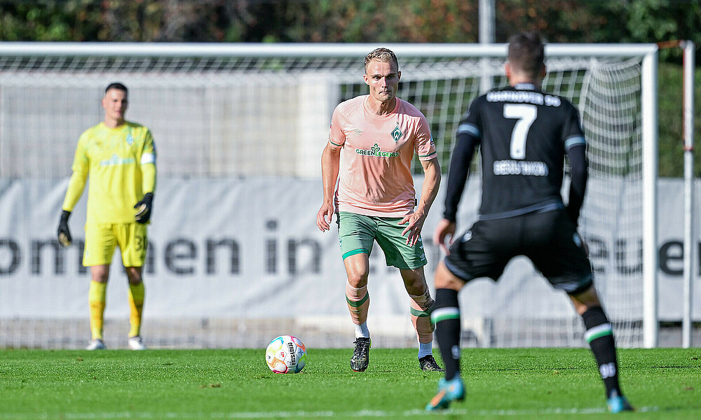 null Amos Pieper mit dem Ball am Fuß, im Vordergrund steht zu ihm gedreht ein Hannover-Spieler.
