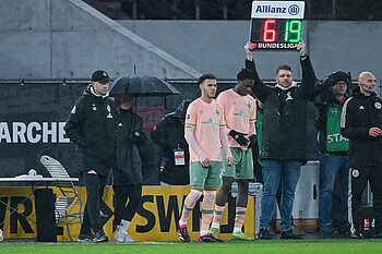 Dikeni Salifou und Lee Buchanan stehen am Spielfeldrand, eine Tafel mit den Zahlen 6 und 19 wird hochgehalten.