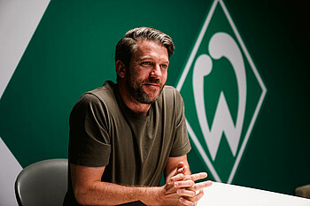 null Peter Niemeyer sitzt an einem Tisch, im Hintergrund die Werder-Raute.