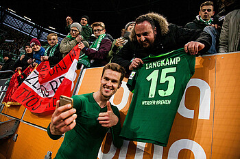 null Sebastian Langkamp macht mit dem Handy ein Foto von sich und einem Fan, der Langkamps Trikot in der Hand hält.