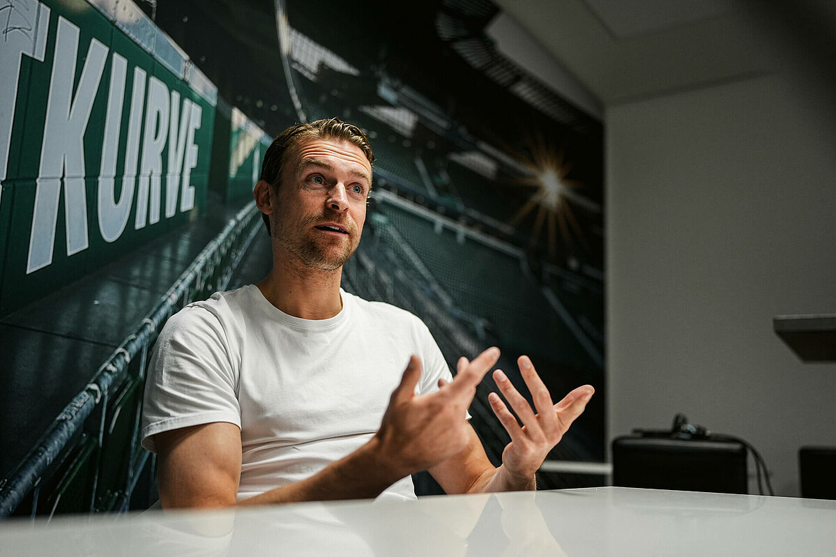 null Oliver Hüsing sitzt an einem Tisch und erklärt.