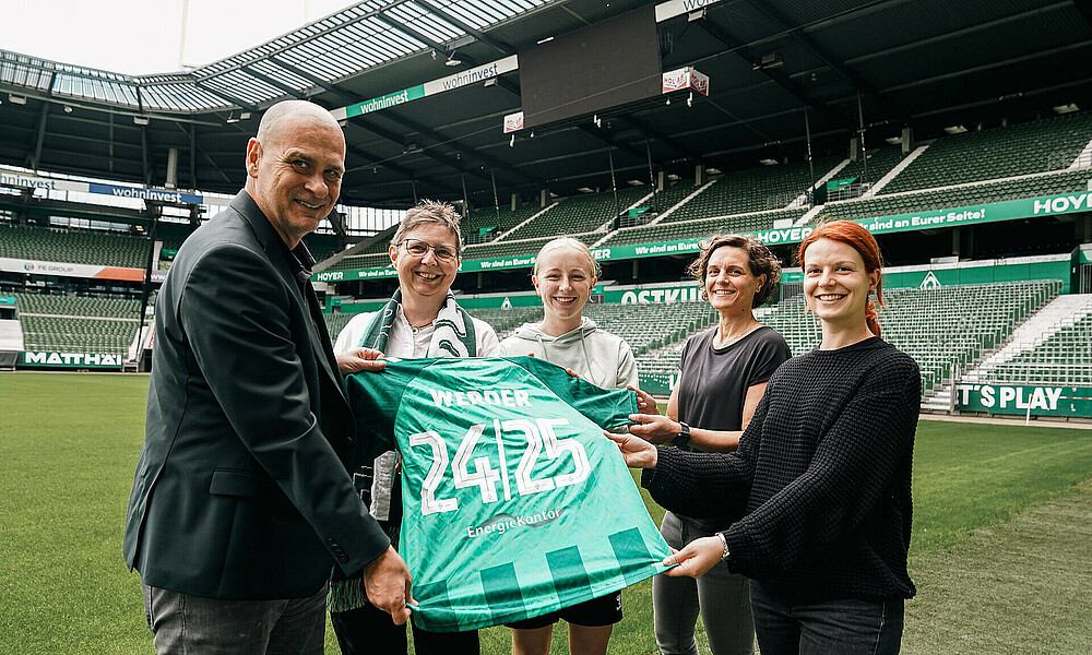 Vertreterinnen von Energiekontor, Klaus Filbry und Caro Siems stehen am Spielfeldrand im Weserstadion.