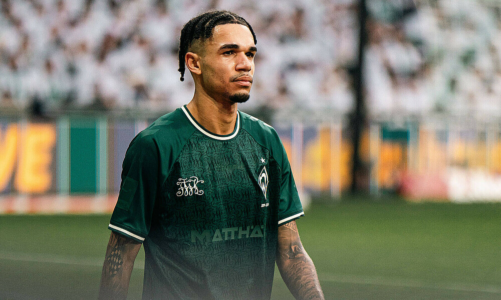 Justin Njinmah läuft mit traurigem Gesicht neben dem Spielfeld. Er trägt das Jubiläumstrikot.