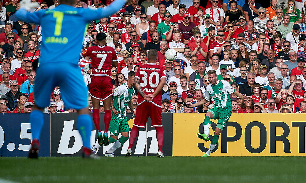 Marvin Ducksch schießt einen Freistoß. Von hinten sind zwei Cottbus-Spieler zu sehen, die eine Mauer bilden. Der Cottbuser Keeper ist von hinten zu sehen. Er hat die Arme ausgebreitet.