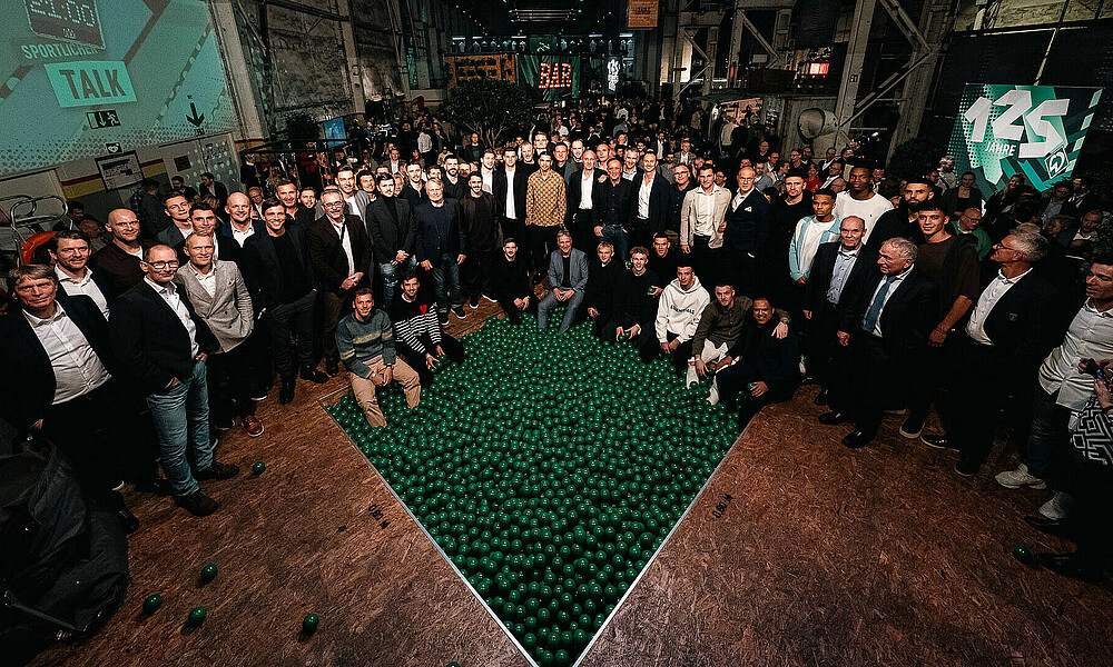 Alle ehemaligen und aktuellen Spieler stehen um ein Bällebad, gefüllt mir grünen Bällen.