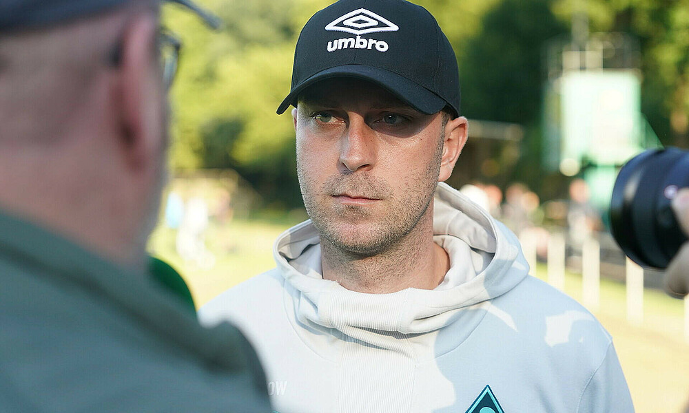 null Ole Werner spricht in ein grünes Mikrofon mit WERDER.TV Aufdruck.