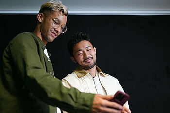 null Yukinari Sugawara und Mio Backhaus schauen in ein Smartphone