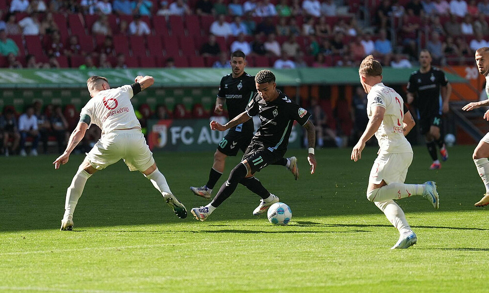 Justin Njinmah mit Ball am Fuß. Um ihn herum stehen zwei Augsburger-Verteidiger.