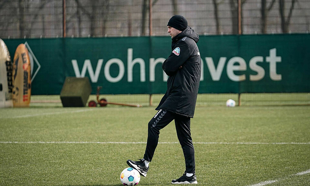 Ole Werner steh auf dem Trainingsplatz. Er hat die Arme verschränkt, ein Bein steht auf einem Ball.