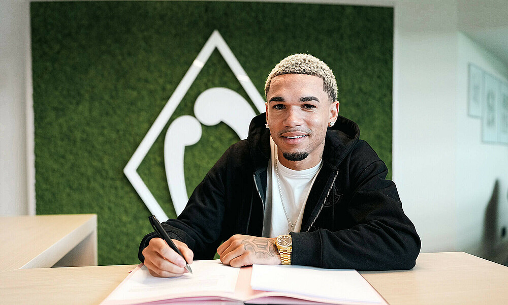 Justin Njinmah unterschreibt seinen Vertrag. 