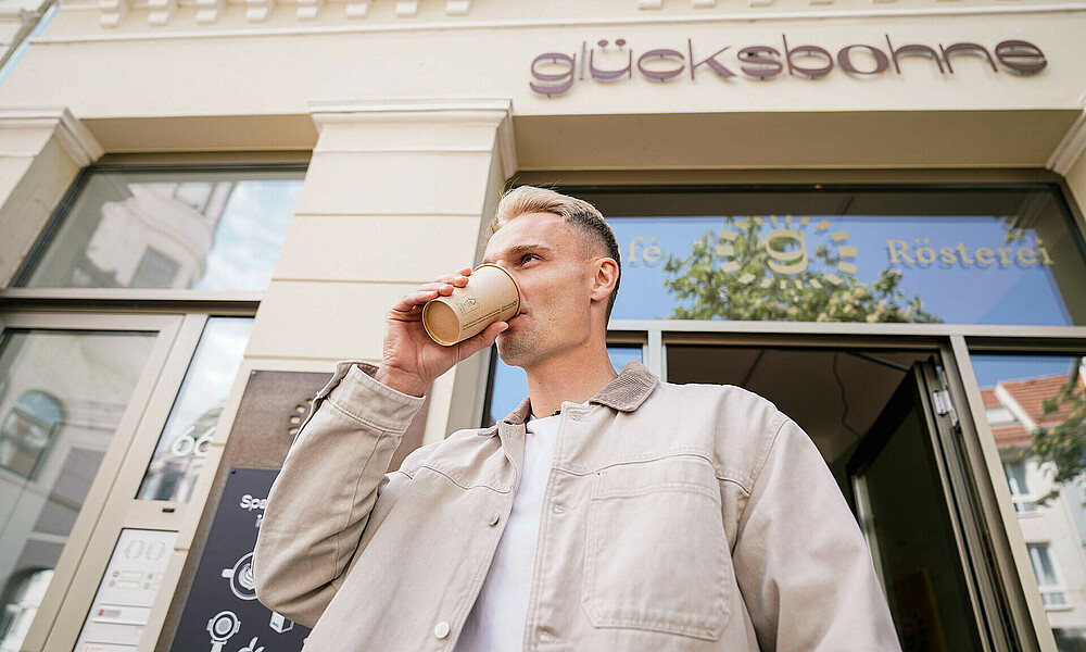 Amos Pieper steht vor dem glücksbohne-Café in Bremen und trinkt einen Kaffee.