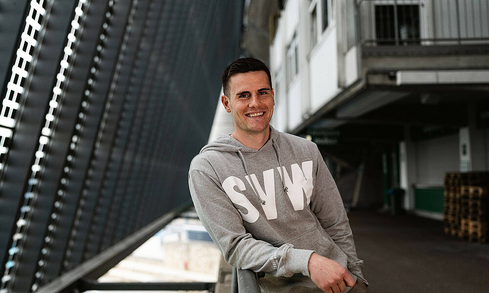 null Michael Zetterer lehnt auf einem Geländer. Er trägt einen grauen Hoodie mit den weißen Buchstaben S V W. Im Hintergrund ist die Photovoltaik-Anlage zu sehen.