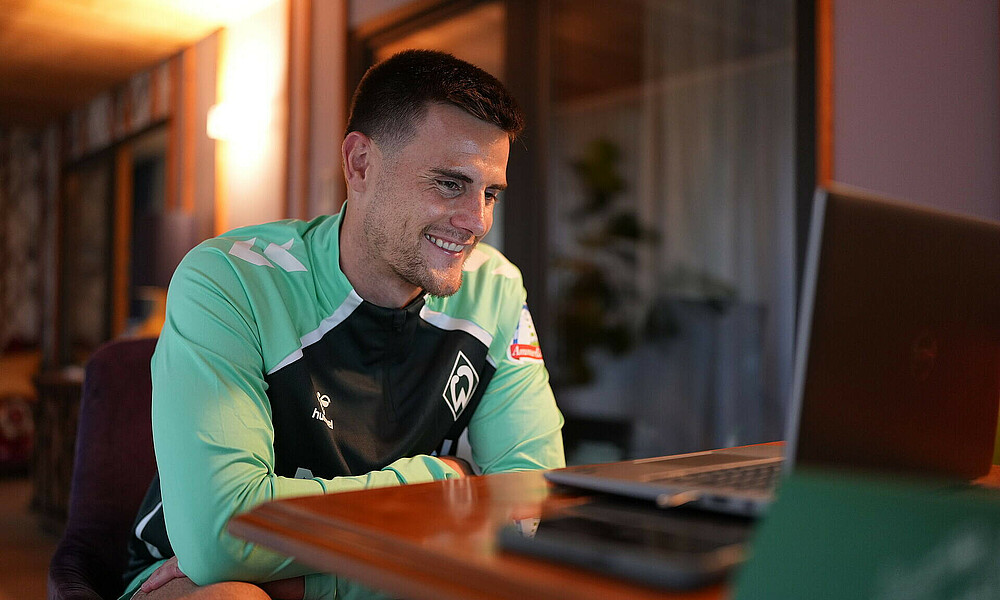 Zetterer sitzt vor einem Laptop und lacht in den Bildschirm.