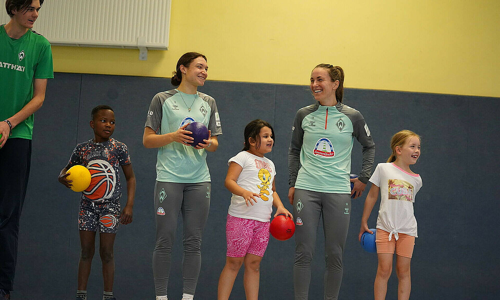 Michaela Brandenburg und Sophie Weidauer stehen zwischen Kindern in einer Sporthalle