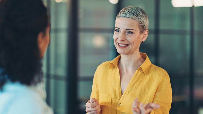 Markt Insights Kapitalmarkt Insights - Businessfrau mit gelber Bluse im Gespräch mit anderer Frau