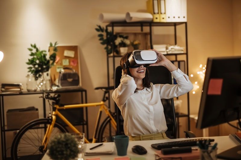Raiffeisen-MegaTrends-ESG-Aktien: Frau sitz lachend in ihrem Büro und arbeitet mit ihrer VR-Brillle