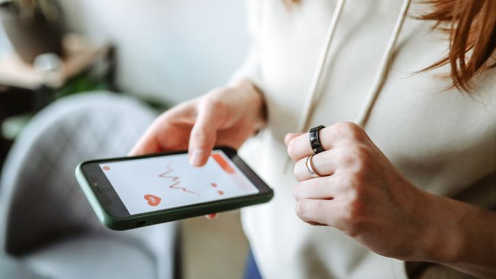 Fitness Tracker Gesund altern - Longevity: Frau hält Smartphone in der rechten Hand und schaut auf Fitness Tracker