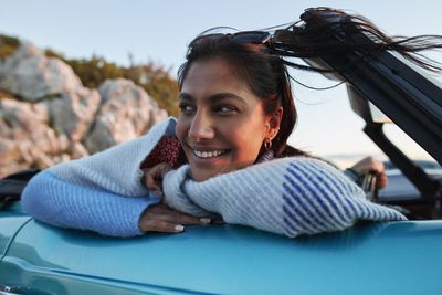 Junge Frau sitzend im Auto glücklich nachdenkend über ihre finanzielle Zukunft