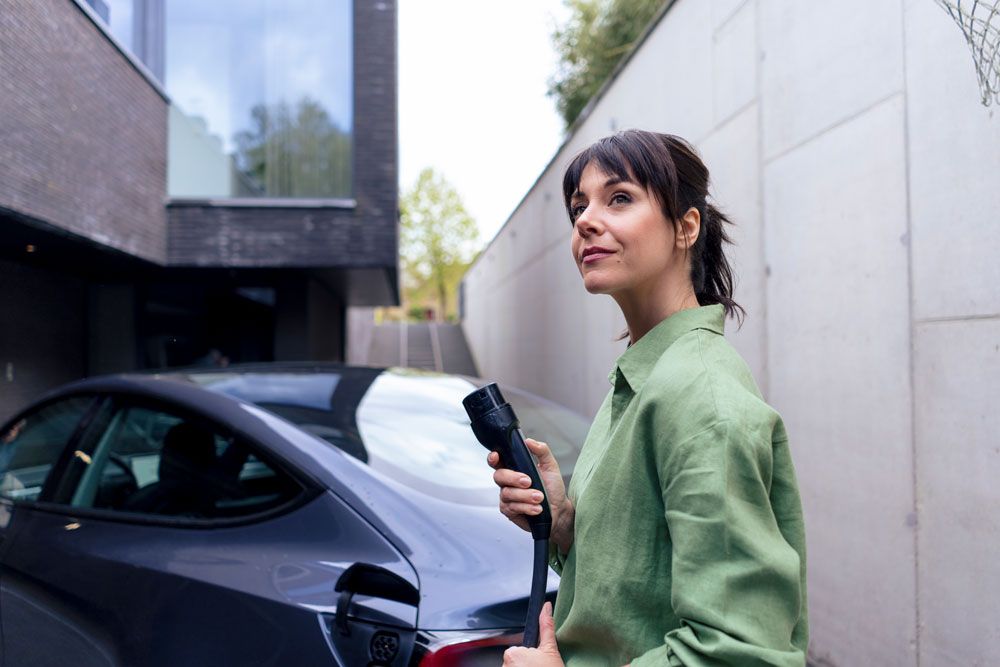 Private Infrastructure Electric Mobility - Thoughtful woman holding the charging cable of her electric car in her hand.