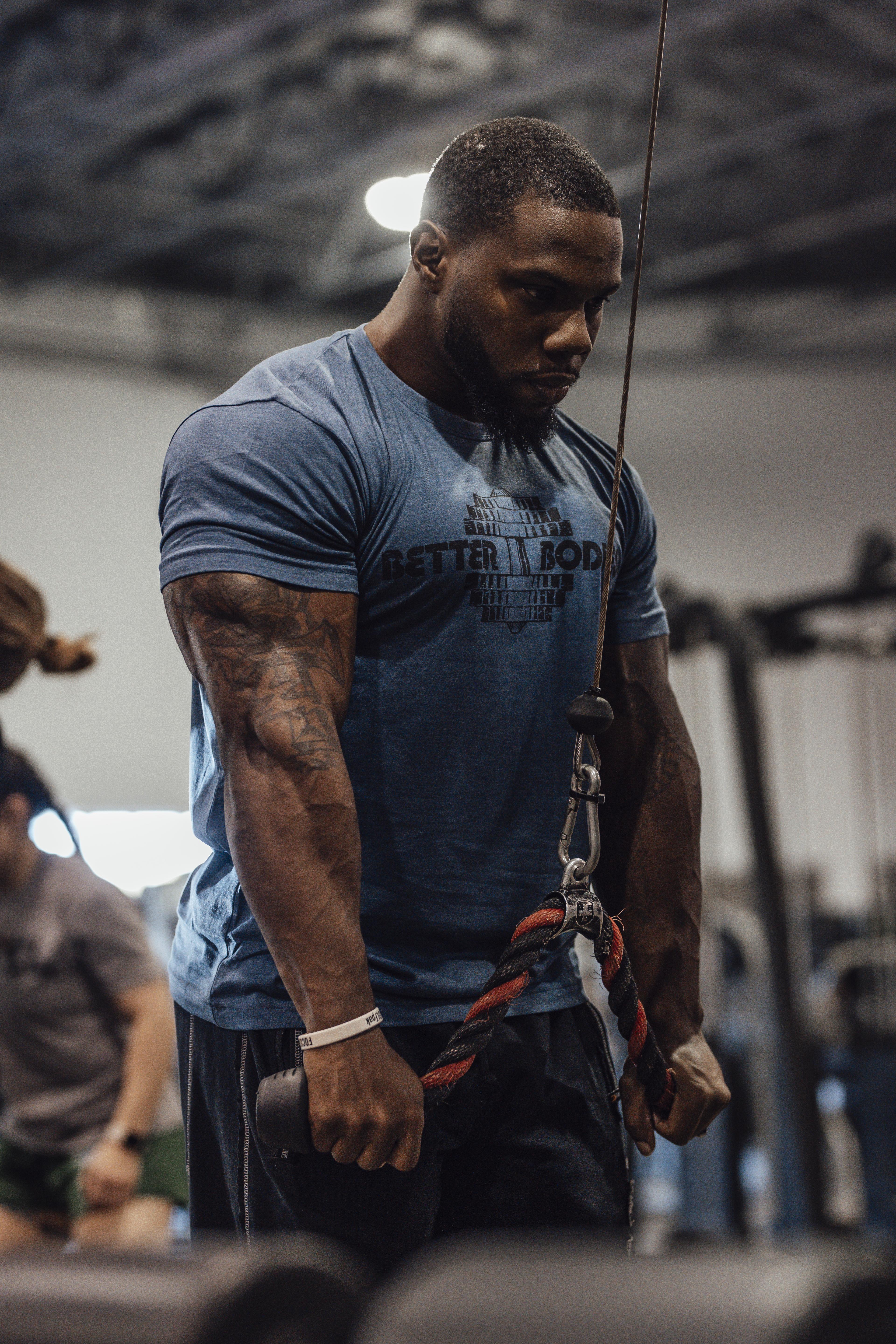 Man in a blue shirt performing a cable tricep pushdown exercise in a gym, with focus and determination.