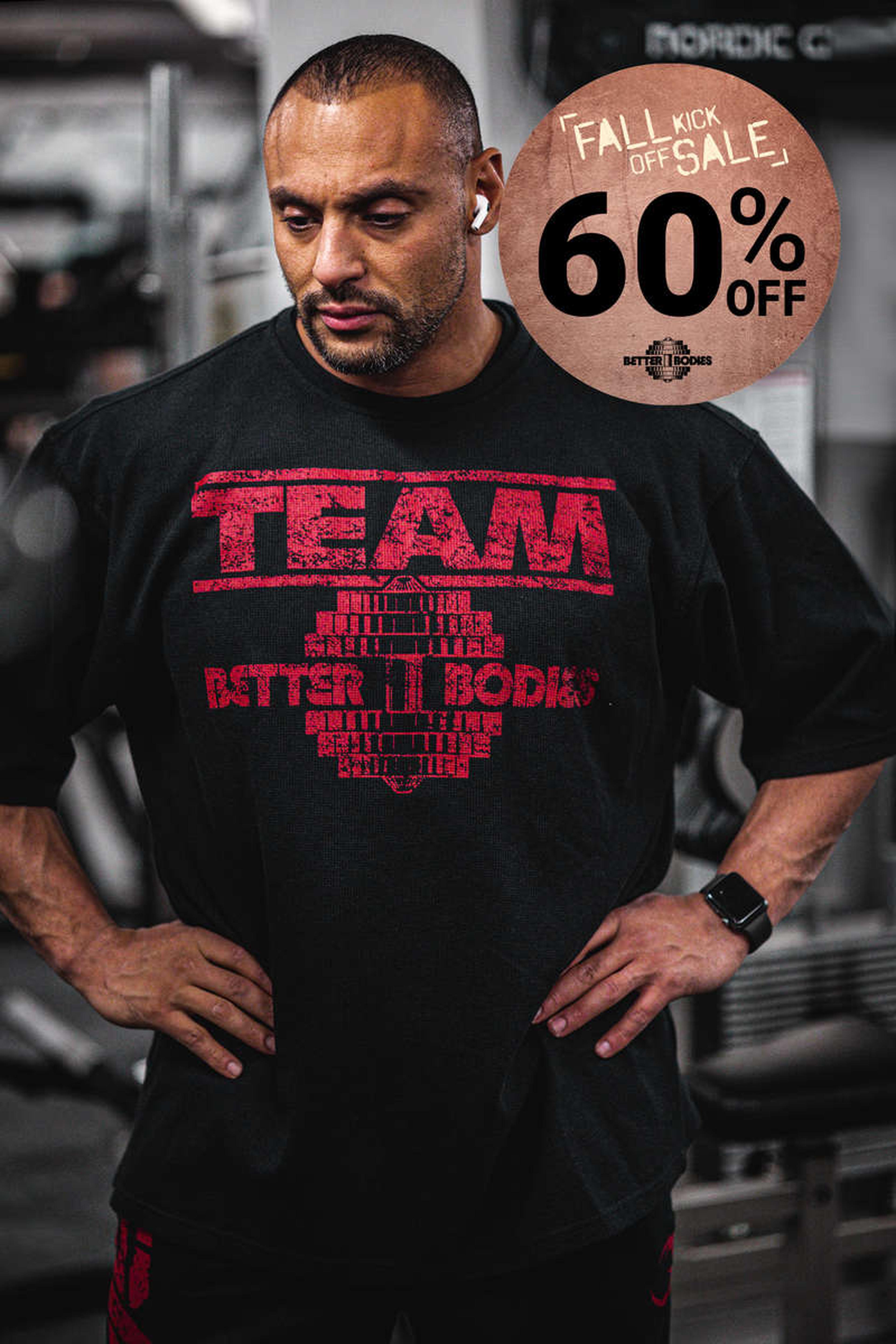 Man in a gym wearing a "TEAM" shirt, with earbuds and a smartwatch. A "Fall Kick Off Sale, 60% Off" sign is visible in the background.