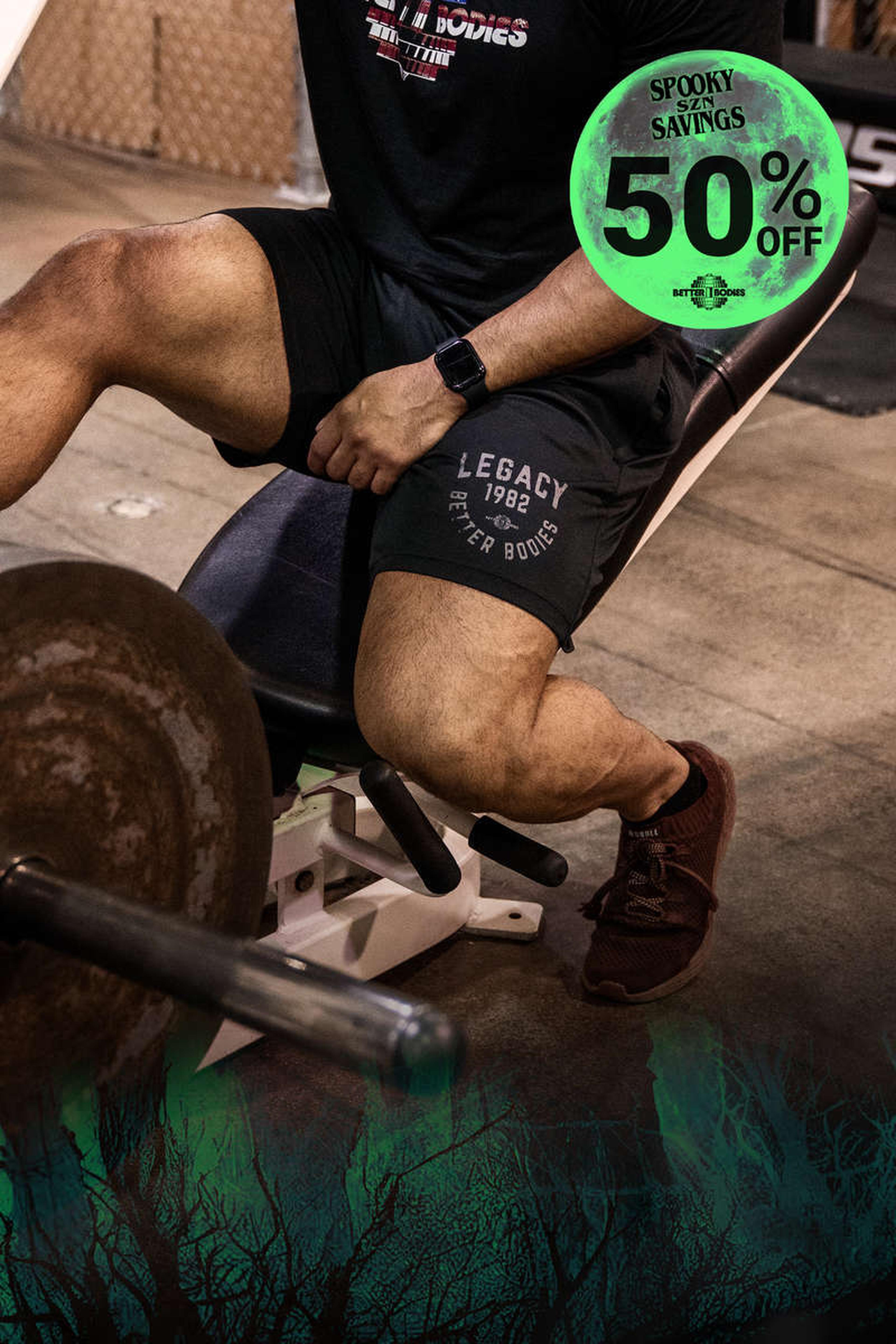 Person sitting on gym equipment with a barbell nearby. "Spooky Savings 50% Off" text overlay with a green tree branch design.