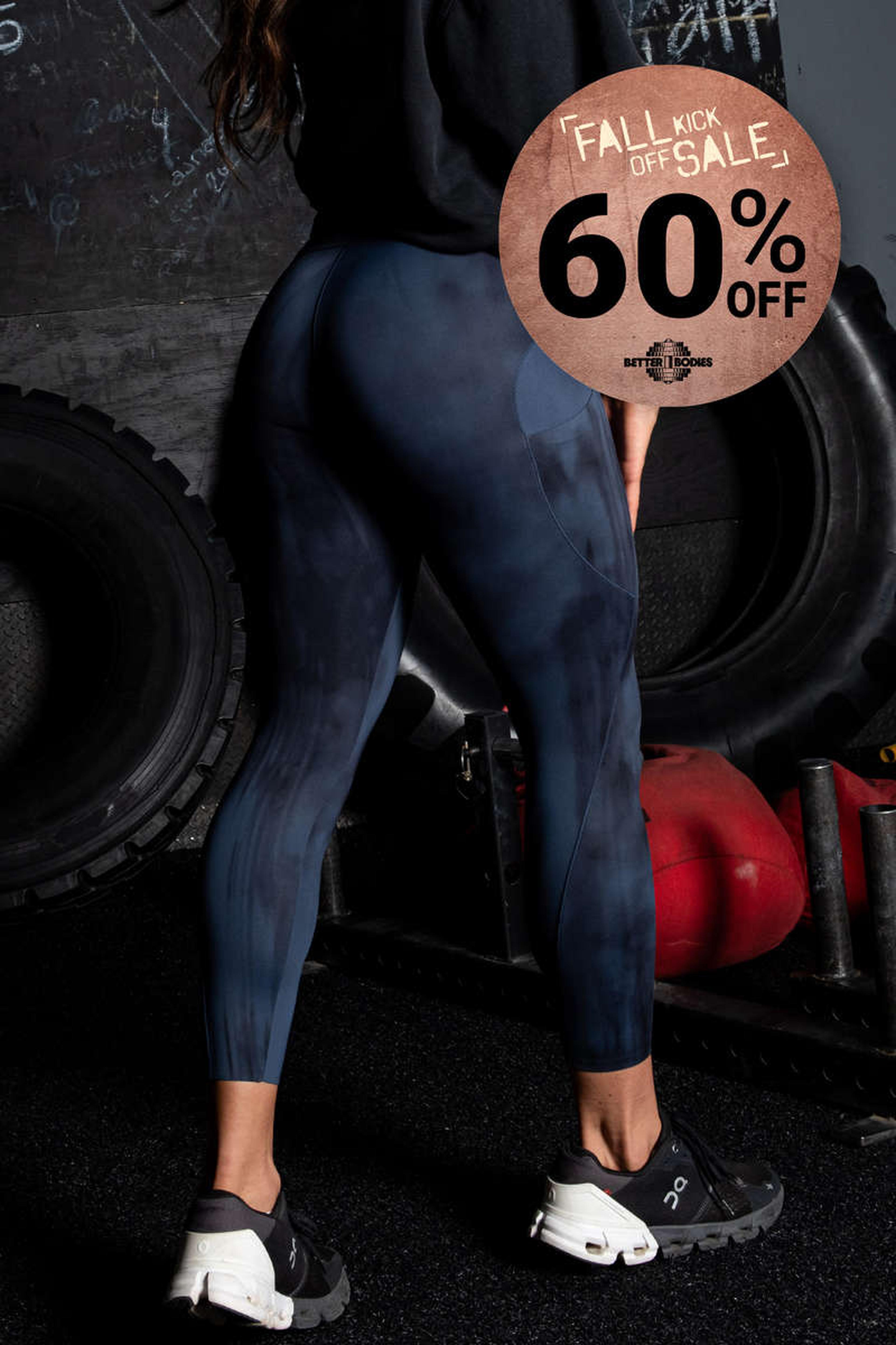 Person in a gym wearing dark leggings and sneakers, standing near large tires. A "Fall Kick Off Sale, 60% Off" sign is displayed.