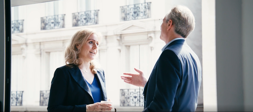 Zwei Personen in einem Gespräch vor einem Fenster.