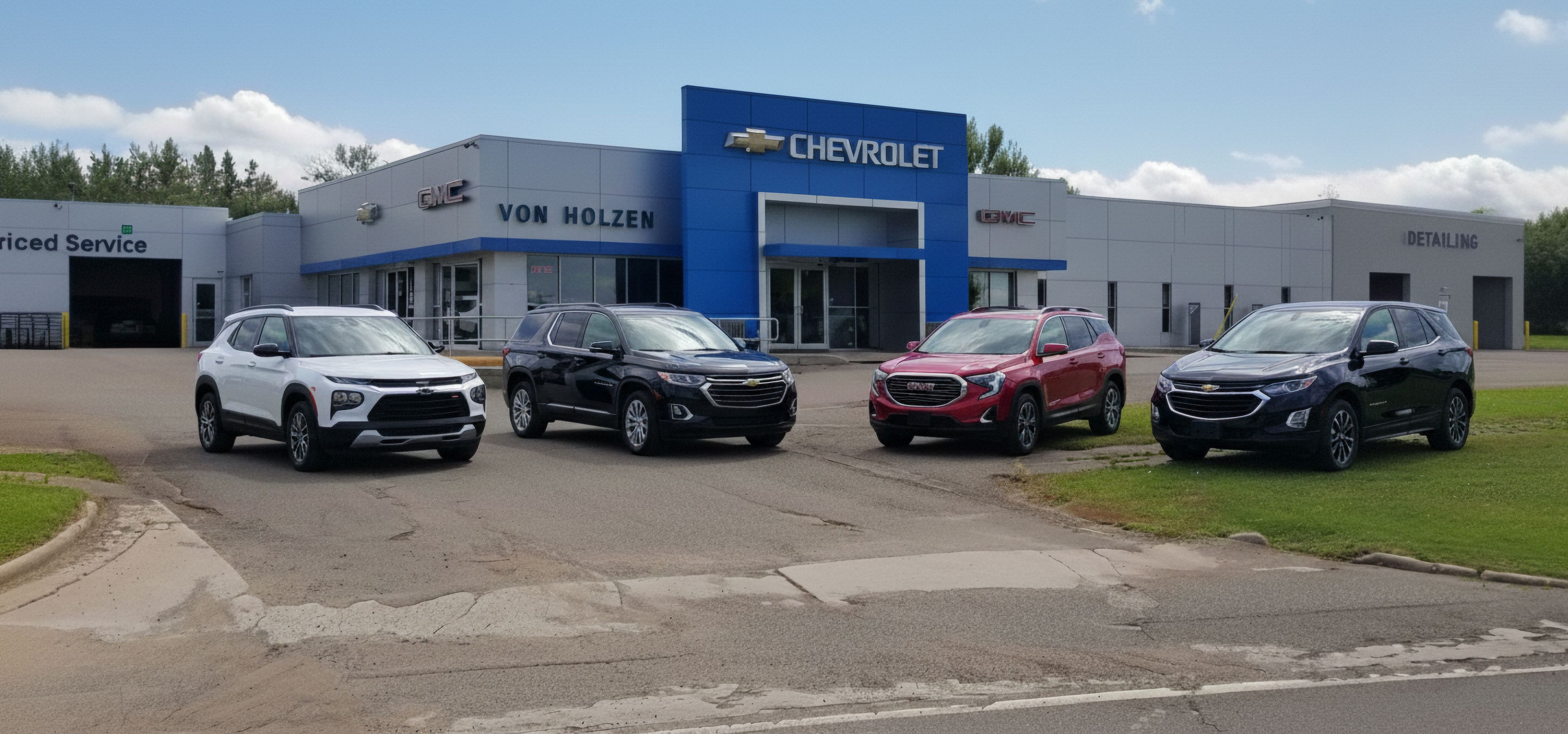 Chevrolet dealership with blue sign and four SUVs (white, black, red, black) lined up in front.
