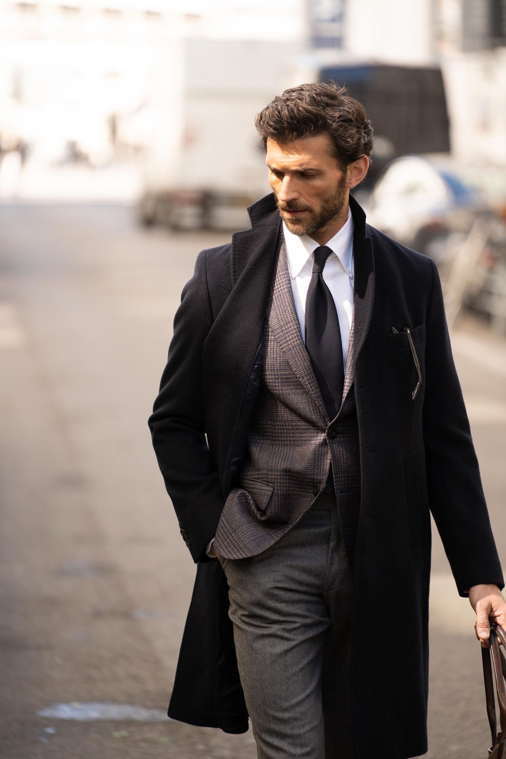 A man in a suit and overcoat walks down the street, holding a briefcase, with a focused expression.