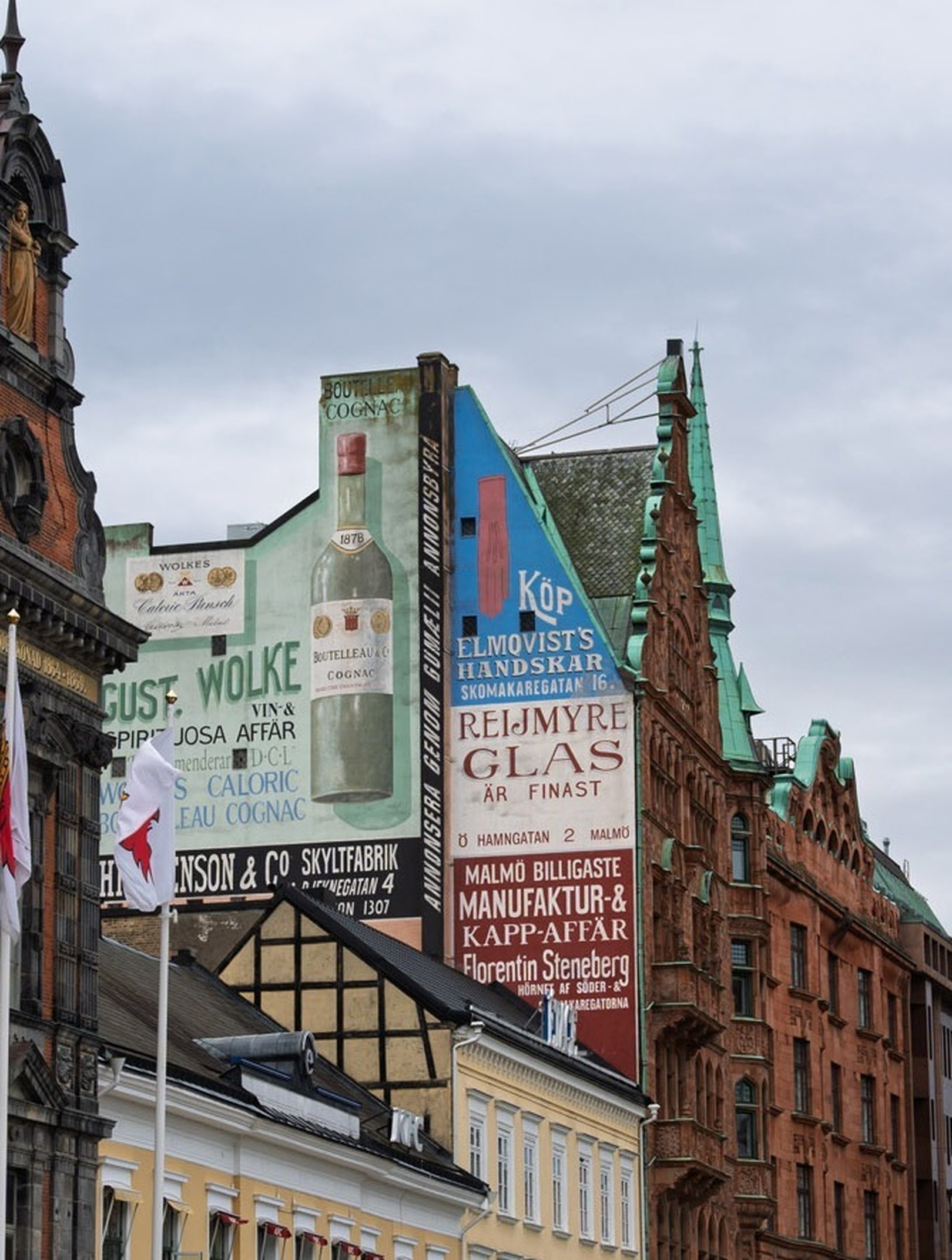 Historic buildings with ornate architecture and vintage advertisements on their facades under a cloudy sky.